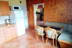 A compact kitchen with a refrigerator, microwave, and a kettle on the counter. There is a dining area with a table and two chairs. - Holiday home in Křemže with Wi-Fi and parking (Křemže)