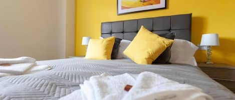 A hotel room with a bed, two pillows, a nightstand, and a lamp.