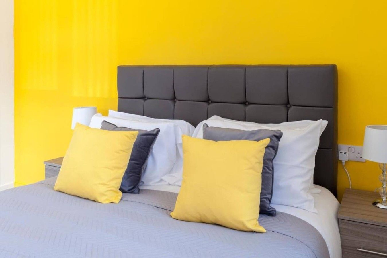 A bed with a grey headboard, white and yellow pillows, and a grey bedspread.