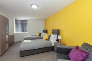 A bedroom with two beds, a wardrobe, a nightstand, and a window with blinds. - SAV Clarence Apt, Loughborough - 2-Bed Charlies (Leicestershire)