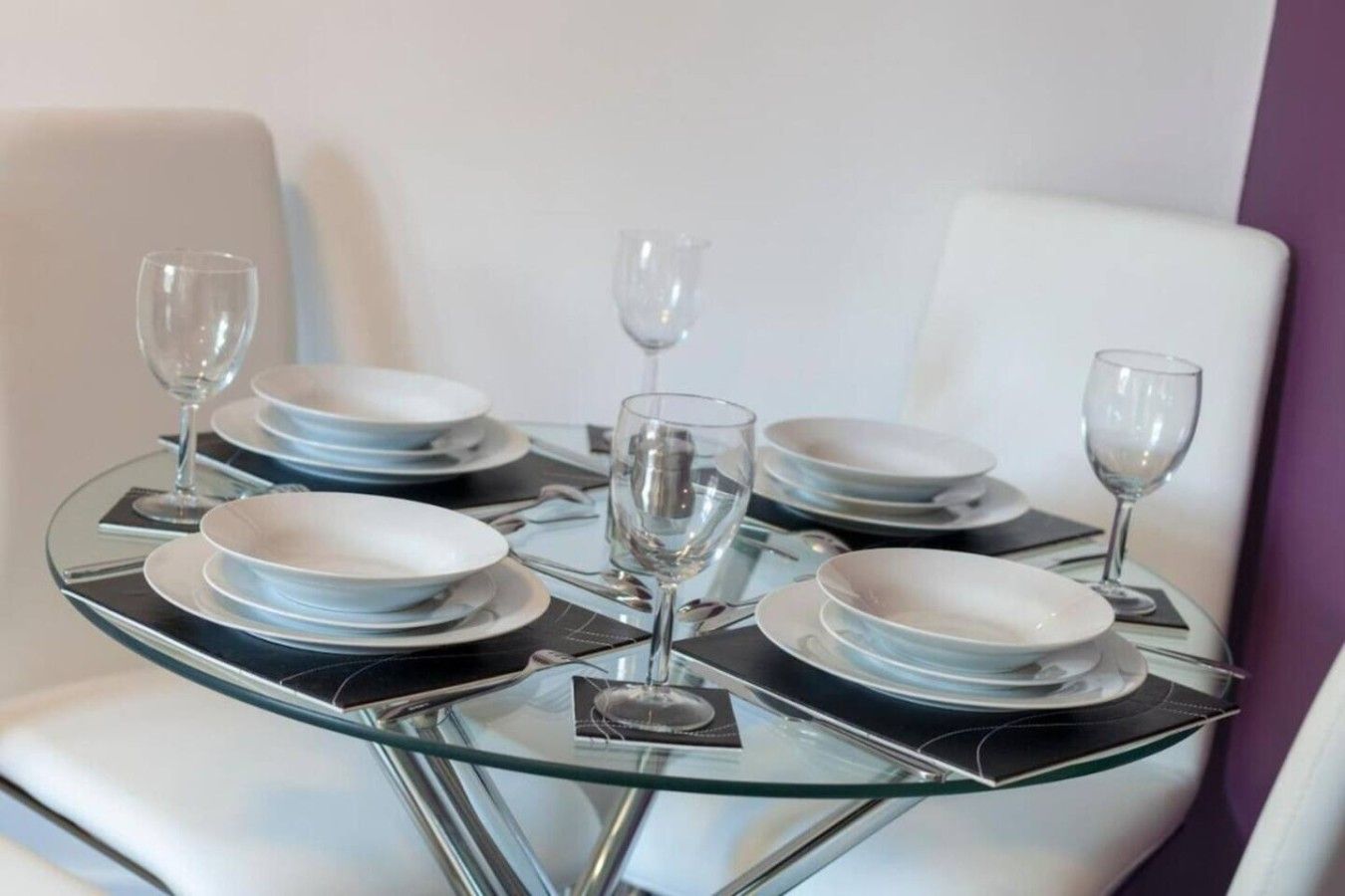A dining table set with plates, cutlery, and glasses, surrounded by white chairs.