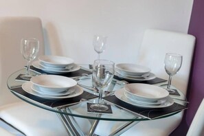 Une table à manger dressée avec des assiettes, des couverts et des verres, entourée de chaises blanches.
