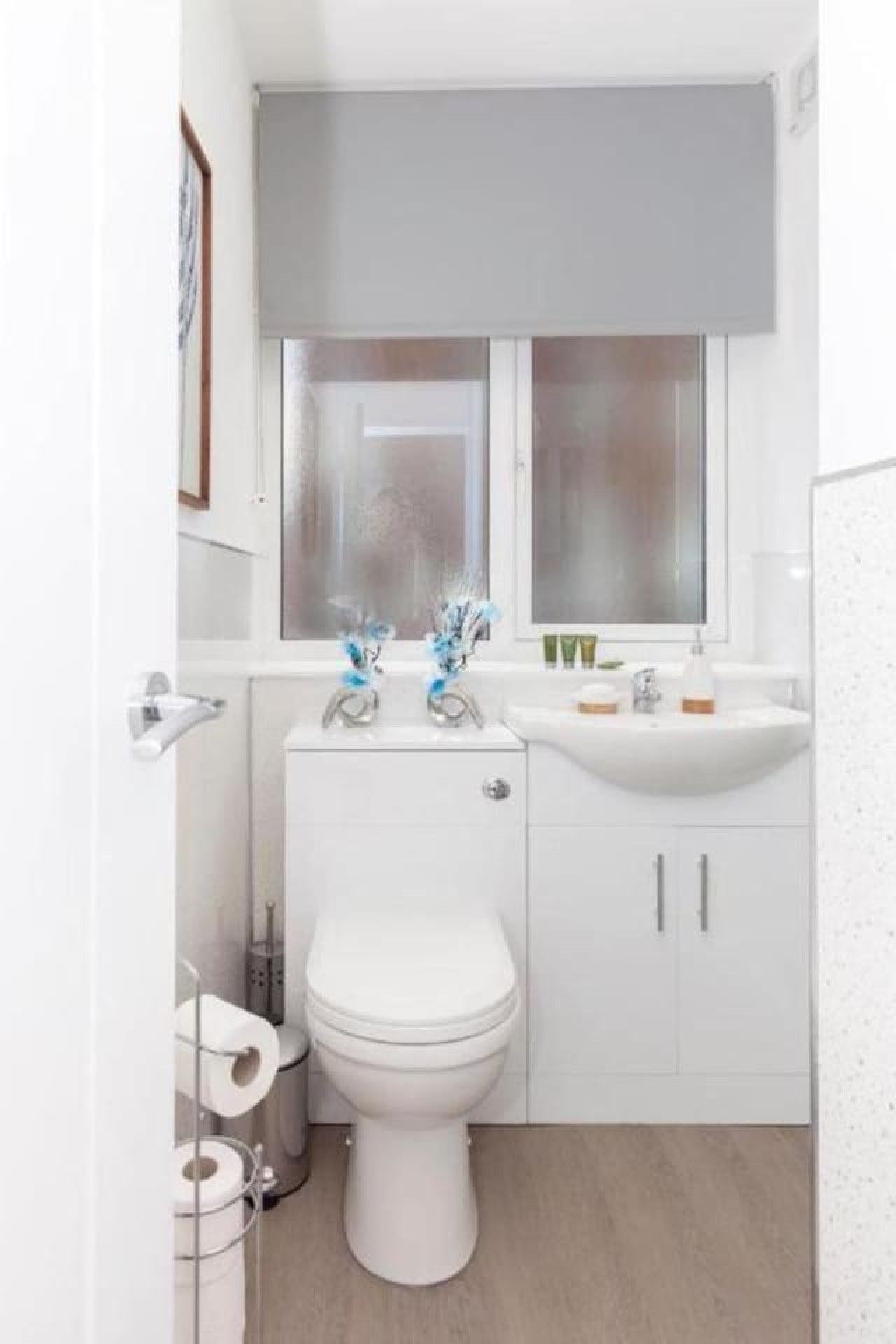 A compact bathroom with a toilet, a sink, and a window above the mirror.