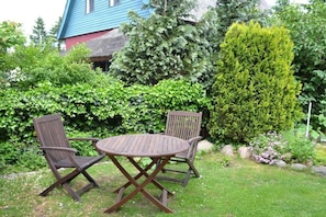 A garden with a round wooden table and two chairs, surrounded by lush greenery and a variety of plants. - Holiday apartment with 1 bedroom (Wieck a. Darss)