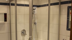 Ducha en esquina con mampara de vidrio, cabezal de ducha manual y una toalla roja colgada en la pared.
