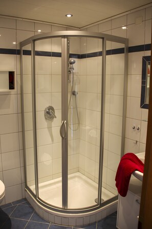 Eine Eckdusche mit Glastür, eine Handbrause und ein rotes Handtuch an der Wand.