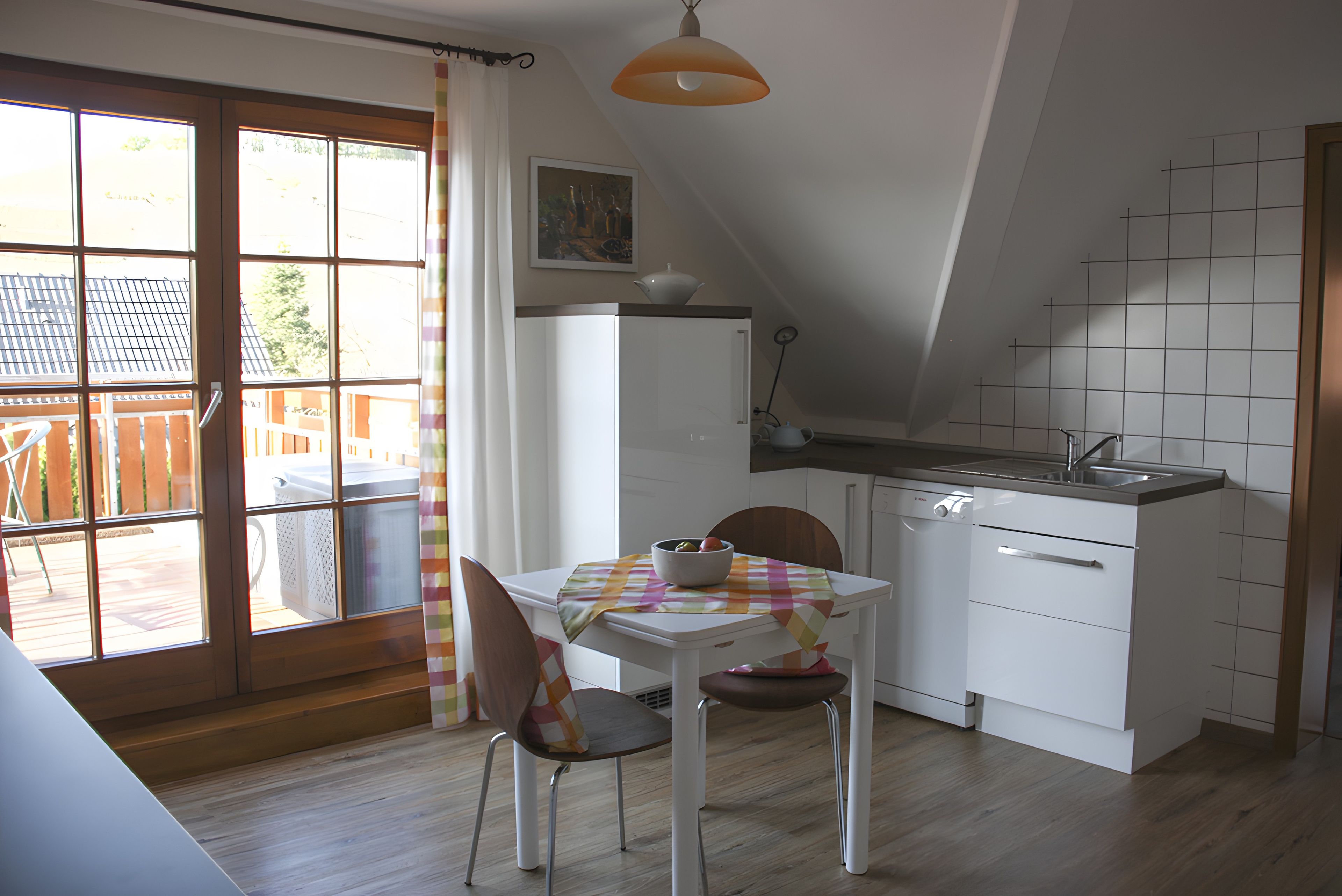 Een kleine keuken met een eethoek, een raam met gordijnen en uitzicht op het buitenland.
