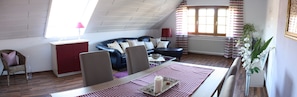 Ein Zimmer mit einer schwarzen Ledersofa, einem Esstisch mit kariertem Tischläufer, einem roten Schrank und einem Fenster mit gestreiften Vorhängen.