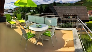 Un balcón con una mesa y sillas, un paraguas verde y vistas a un paisaje verde.