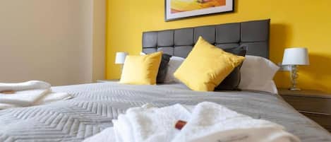A hotel room with a bed, two pillows, a bedside lamp, and a painting on the wall.