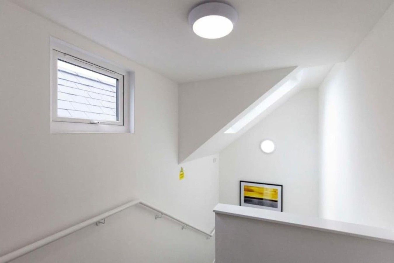 A stairwell with a window, a framed picture, and a ceiling light fixture.