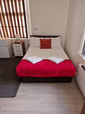 Une chambre d’hôtel avec un lit, une table de chevet, une lampe et une fenêtre avec des stores.