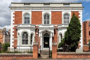 A two-story building with a symmetrical facade, featuring a central entrance with a black door, flanked by two arched windows on each side. - Sav Apartments Regent Leicester - Studio (Leicester)