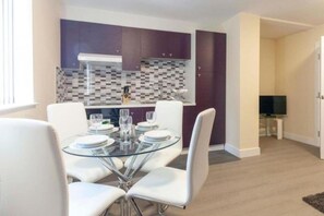 A modern kitchen with purple cabinets, a glass dining table with white chairs, and a tiled backsplash. - SAV Clarence Apt, Loughborough - 3-Bed Generals (Leicestershire)