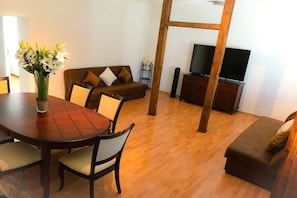 Ein Wohnzimmer mit Holzboden, einem runden Esstisch mit Stühlen, einer Couch, einem Fernseher und einer Holzleiter.
