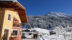 A two-story building with a balcony, a mountain in the background, and snow-covered surroundings. - Large apartment for 2 families (Kleinarl)