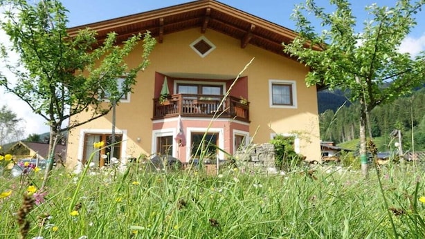A two-story building with a balcony, surrounded by greenery and mountains in the background. - Large apartment for 2 families (Kleinarl)