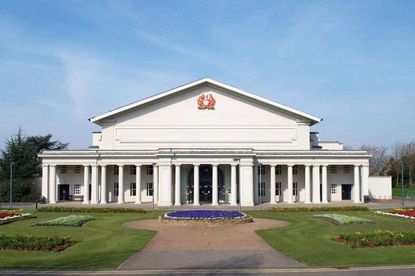 A large, white building with a central entrance flanked by columns, a symmetrical facade, and a formal garden with a central water feature.