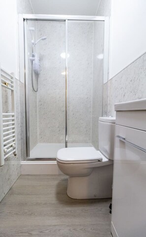 Une salle de bain avec une douche à parois de verre, des toilettes et un meuble de rangement.