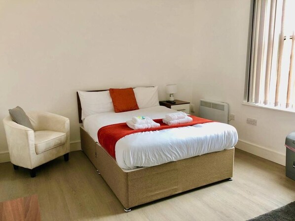 Une chambre d’hôtel avec un lit, une chaise, une table de chevet et une fenêtre.