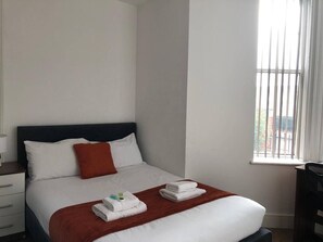 Ein Hotelzimmer mit einem Bett, einem Nachttisch, einem Fenster mit Jalousien und einem Sessel.