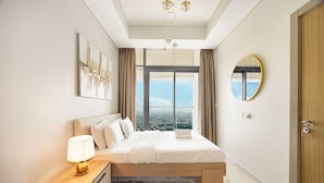 A hotel room with a large bed, a bedside table with a lamp, a view of the city through the window, and a round mirror on the wall. - Aykon City 2BR High Floor Business Bay (Dubai)