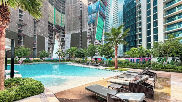 A swimming pool with lounge chairs and a palm tree, surrounded by high-rise buildings. - Aykon City 2BR High Floor Business Bay (Dubai)