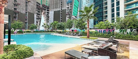 A swimming pool with lounge chairs and a palm tree, surrounded by high-rise buildings.