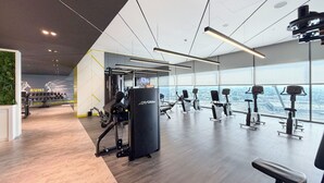 A modern gym with various exercise equipment, a mirrored wall, and a view of the city through large windows. - Aykon City 2BR High Floor Business Bay (Dubai)
