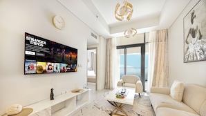 A modern living room with a flat-screen TV, a sofa, a coffee table, and a large window offering a view. - Aykon City 2BR High Floor Business Bay (Dubai)