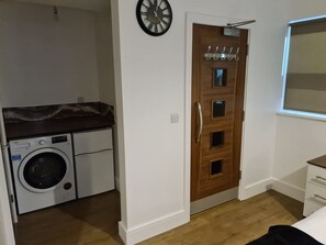 Una habitación compacta con lavadora, una puerta de madera con perchero y un ventanal pequeño.