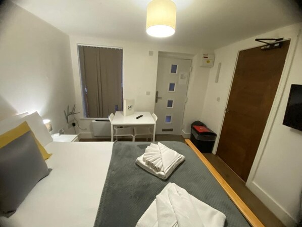 Une chambre d’hôtel avec un lit, un bureau, une chaise, une télévision, une porte et une fenêtre.