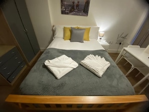 A neatly made bed with folded towels, a bedside table with a lamp, and a wardrobe. - Sav | Regent | Leicester-Studio Walking to Demont (Leicester)