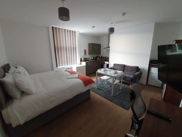 Une chambre d’hôtel moderne équipée d’un lit, d’une table à manger avec des chaises, d’un canapé, d’une télévision et d’un coin cuisine.