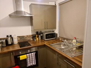 A compact kitchen with a stainless steel range hood, a microwave, and a sink. - Sav Apartments Regent Leicester - 2 Bed Flat (Leicester)