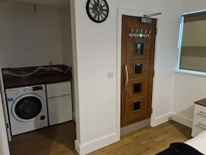Ein kleines Zimmer mit Waschmaschine, einer Holztür und einem kleinen Fenster.