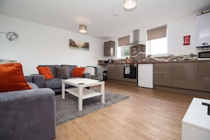 Ein modernes Wohnzimmer mit einem grauen Sofa, einem weißen Couchtisch und einer Küchenzeile inklusive Herd, Backofen und Mikrowelle.