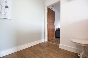 Ein Flur mit Holzboden, einer weißen Wand und einer Tür zu einem Raum mit einem grauen Sofa.