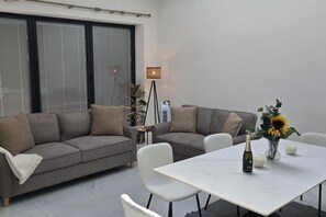 A modern living room with a grey sofa, a white table, and a vase with a sunflower.