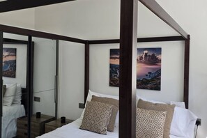 A bedroom with a four-poster bed, a glass door leading to a balcony, and two landscape paintings on the wall.