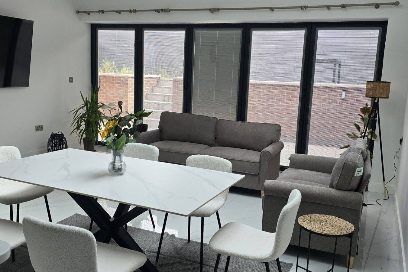 A modern living room with a white marble table, grey sofas, and a large window with blinds.
