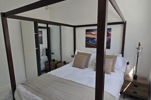 A four-poster bed with a mirror cabinet, a bedside lamp, and two paintings on the wall.