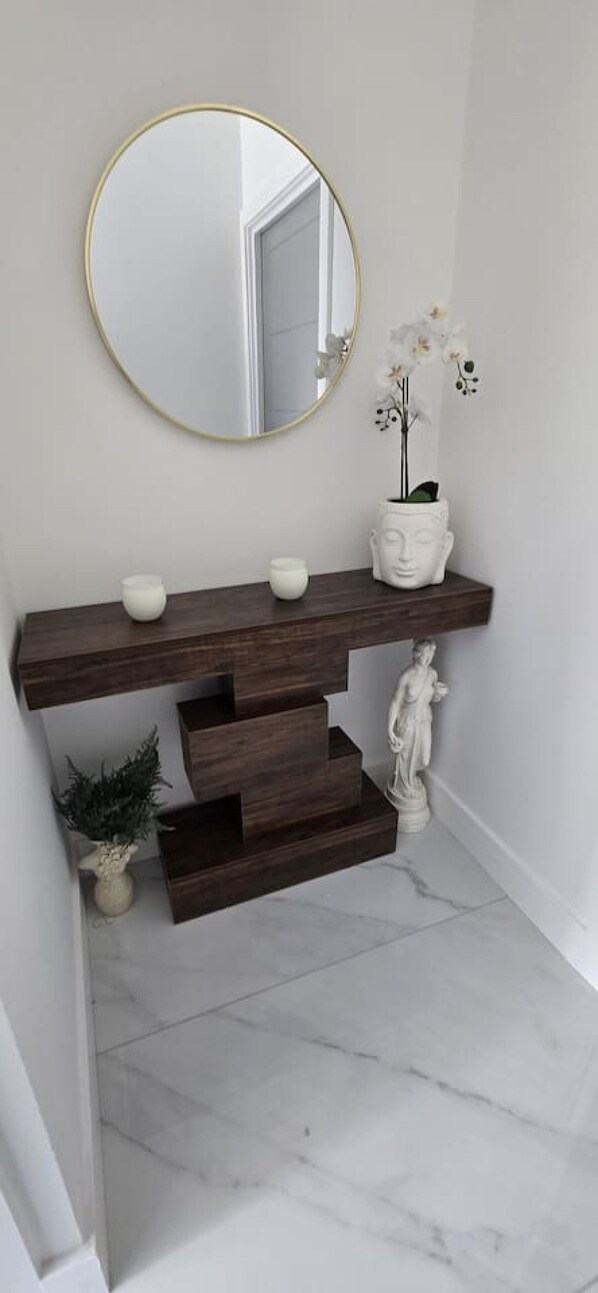 A bathroom vanity with a round mirror, a white vase, and a statue.
