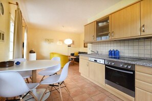 A compact kitchen with a dining area, wooden cabinets, a stove, and a tiled backsplash. - Holiday apartment with 2 bedrooms (Ostseebad Prerow)