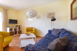A living room with a sofa, yellow armchair, white coffee table, bookshelf, and a flat-screen TV. - Holiday apartment with 2 bedrooms (Ostseebad Prerow)