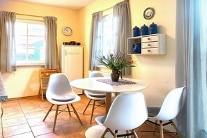 A dining area with a round table and four chairs, a potted plant, a white cabinet with blue containers, and a clock on the wall. - Holiday apartment with 2 bedrooms (Ostseebad Prerow)