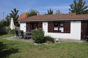 Ein eingeschossiges Gebäude mit Ziegeldach, einer kleinen Terrasse mit Tisch und Stühlen sowie einem Grill.