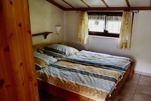 A bedroom with a wooden bed, a window with curtains, and a wall-mounted light fixture. - Zeebos Holiday Park 24 (Bredene)