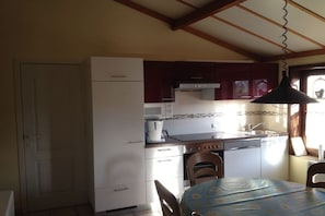 A compact kitchen with a dining table, a refrigerator, a stove, and a hanging light fixture. - Zeebos Holiday Park 24 (Bredene)