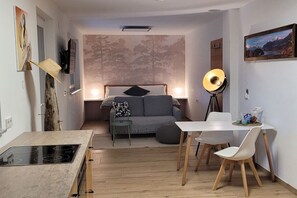 En kompakt opholdsstue med tekøkken, sofa, spisebord og et stort vindue.